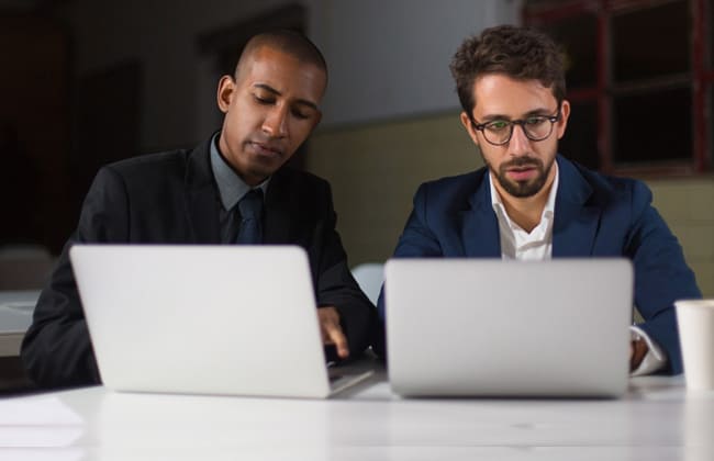 Two professionals working together on laptops at a table